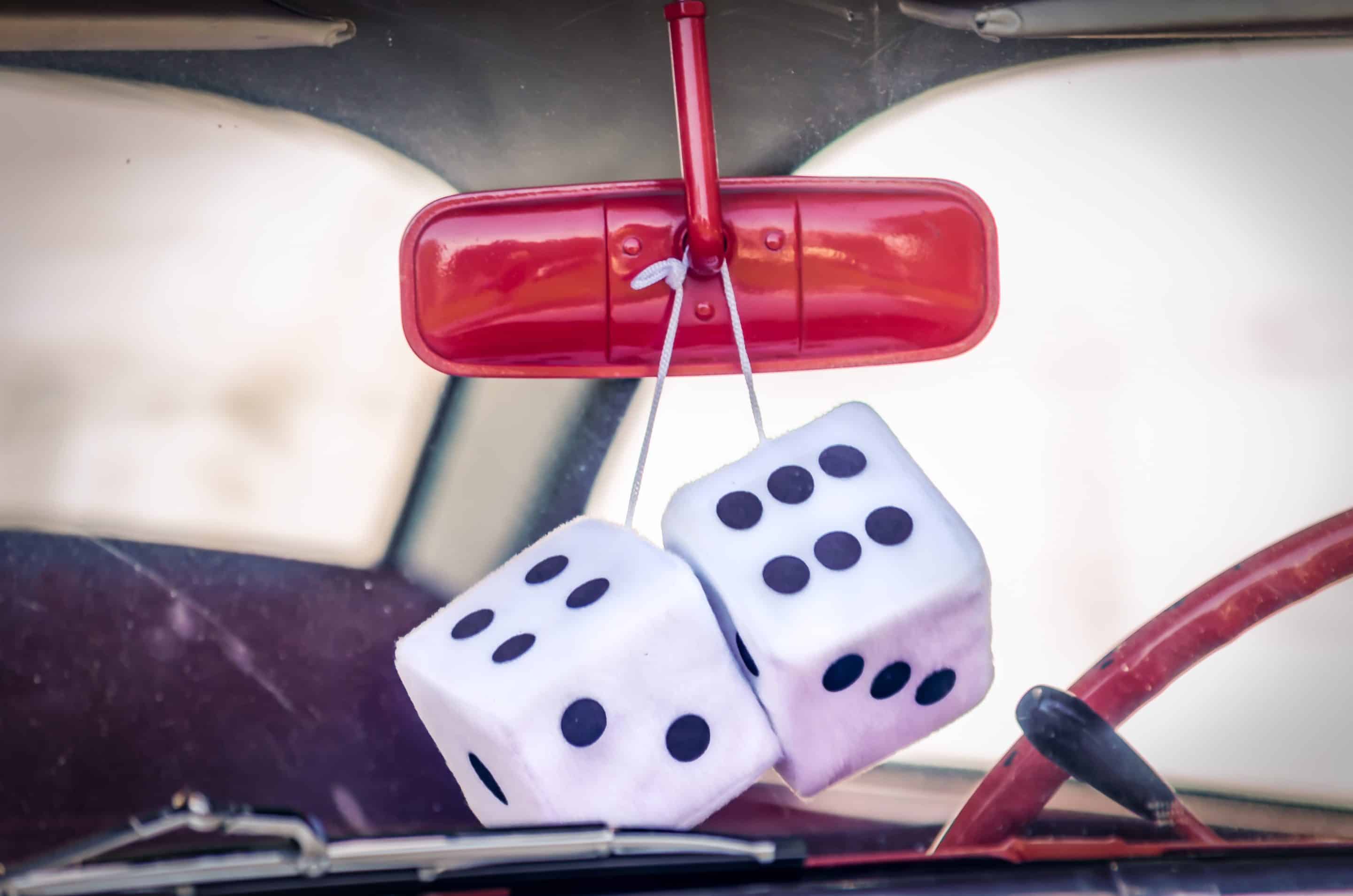 Antique car with red rearview mirror and large white fuzzy dice hanging.
